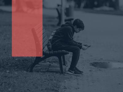 Foto af ensom dreng på en bænk med sin telefon